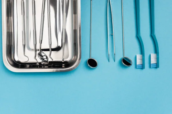 Vue du dessus des brosses à dents et des outils dentaires sur fond bleu — Photo de stock