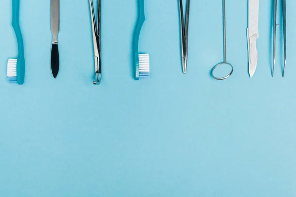 Верхний вид ряда зубных инструментов и зубных щеток на синем фоне с копировальным пространством — стоковое фото
