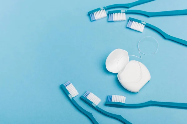 Vue du dessus de la soie dentaire et des brosses à dents sur fond bleu — Photo de stock