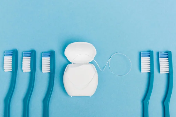 Vue du dessus des brosses à dents et de la soie dentaire sur fond bleu — Photo de stock