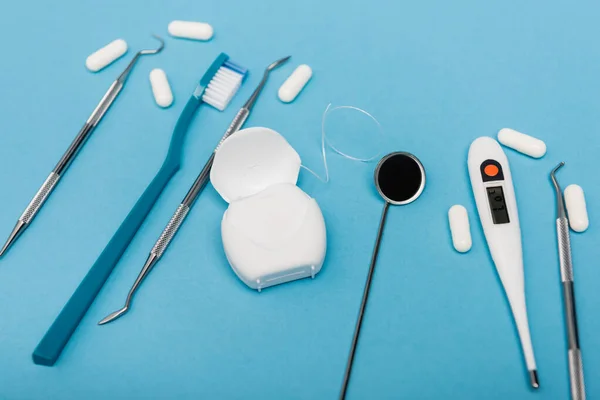 Fio dental perto de ferramentas, termômetro e pílulas em fundo borrado no fundo azul — Fotografia de Stock