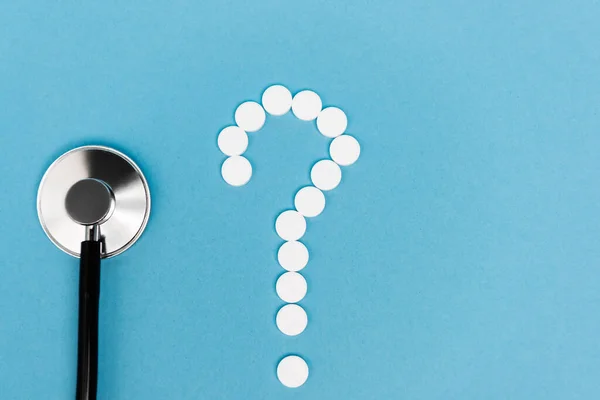 Top view of question sign from pills and stethoscope on blue background — Stock Photo