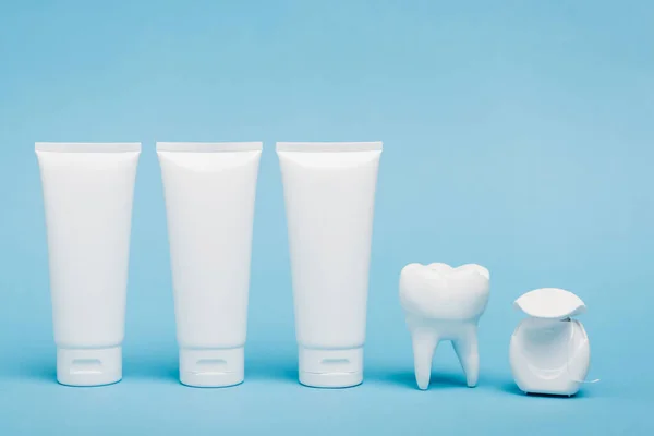 White tubes of toothpaste near tooth model and dental floss on blue background — Stock Photo