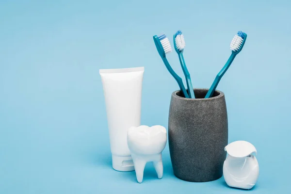 Dentifrice, brosses à dents et fil dentaire près du modèle de dent sur fond bleu — Photo de stock