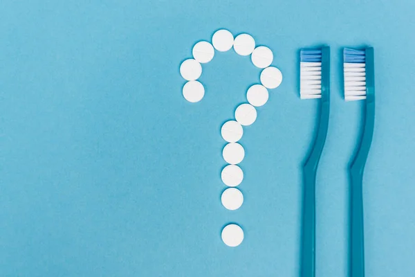 Vue du dessus du signe de question des pilules et des brosses à dents sur fond bleu — Photo de stock