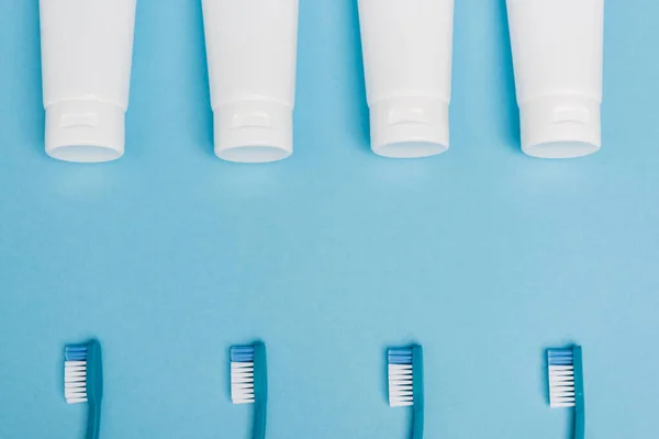 Vista superior de tubos com pasta de dentes e escovas de dentes no fundo azul — Fotografia de Stock