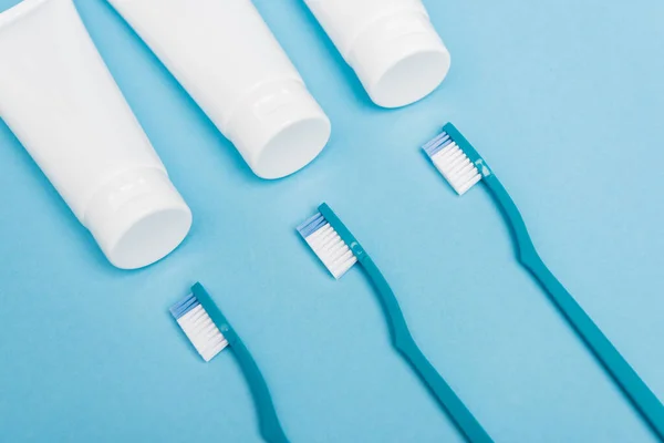 Top view of toothbrushes near tubes with toothpaste on blue background — Stock Photo
