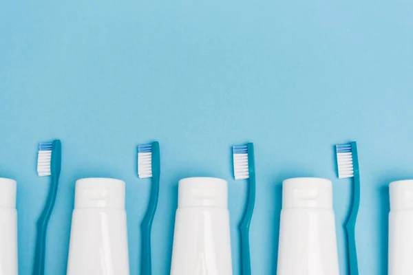 Top view of row of toothbrushes and tubes with toothpaste on blue background — Stock Photo