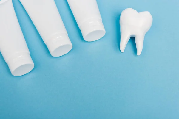 Top view of tooth model and tubes with toothpaste on blue background — Stock Photo