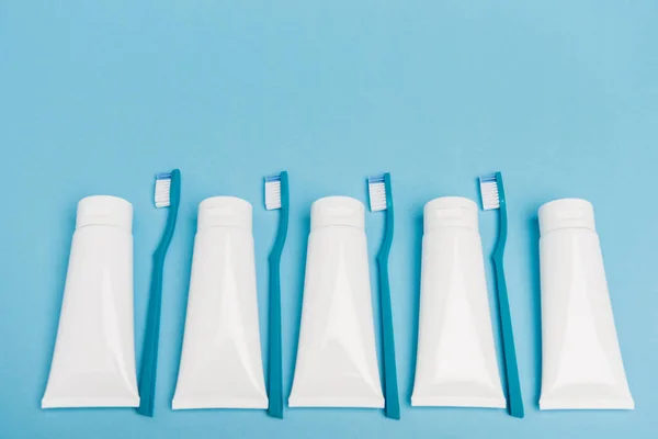 Draufsicht auf blaue Zahnbürsten und weiße Tuben Zahnpasta auf blauem Hintergrund — Stockfoto