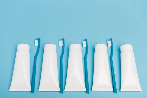 Vue du dessus des brosses à dents bleues et des tubes blancs de dentifrice sur fond bleu — Photo de stock