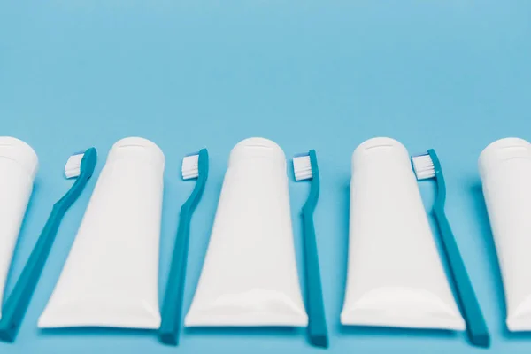 Tubos brancos com pasta de dentes e escovas de dentes em primeiro plano desfocado no fundo azul — Fotografia de Stock