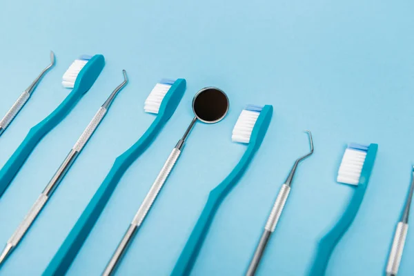 Espelho dentário perto de ferramentas e escovas de dentes em primeiro plano desfocado no fundo azul — Fotografia de Stock