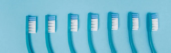 Vista superior de la fila de cepillos de dientes sobre fondo azul, pancarta - foto de stock