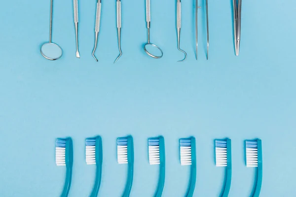 Visão superior das linhas de escovas de dentes e ferramentas odontológicas no fundo azul — Fotografia de Stock