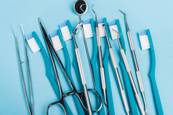 Vista superior de ferramentas dentárias inoxidáveis e escovas de dentes no fundo azul — Fotografia de Stock