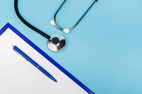 Vue du dessus du stylo et du presse-papiers près du stéthoscope sur fond bleu — Photo de stock