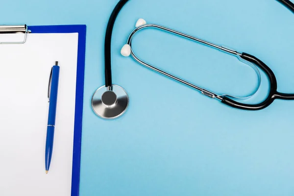 Top view of stethoscope and clipboard with pen on blue background with copy space — Stock Photo