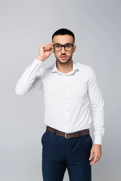 Brunette hispanic businessman adjusting eyeglasses while looking at camera isolated on grey — Stock Photo