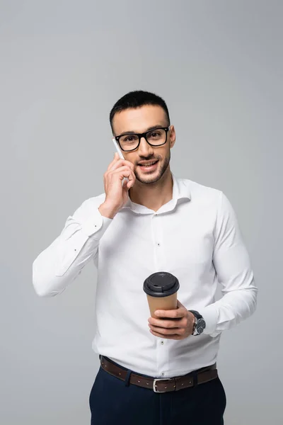 Empresário hispânico alegre com café para ir falar no telefone celular isolado no cinza — Fotografia de Stock
