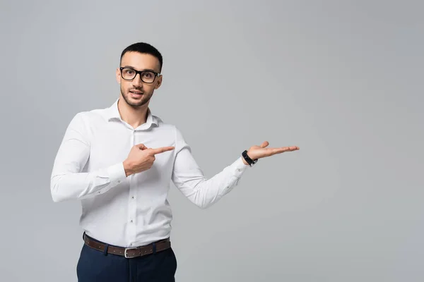 Spanischer Manager in weißem Hemd und Brille blickt in die Kamera und zeigt vereinzelt zur Seite auf grau — Stockfoto