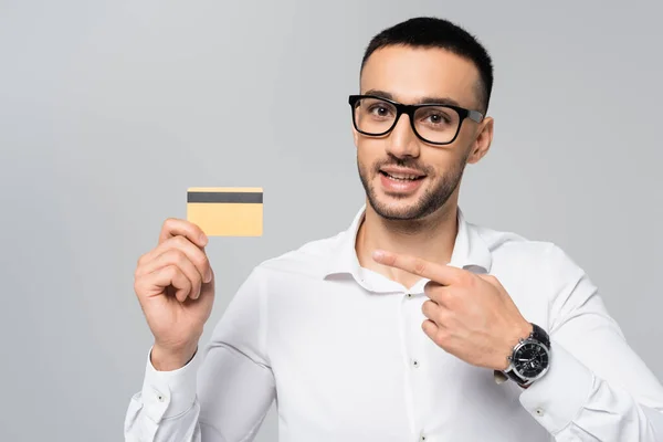 Uomo d'affari ispanico sorridente che punta con il dito alla carta di credito isolata su grigio — Foto stock