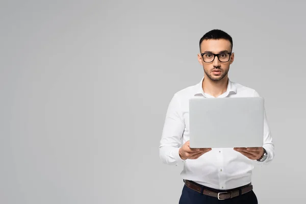 Junger hispanischer Manager mit Brille, Laptop in der Hand und Kamera isoliert auf grau — Stockfoto