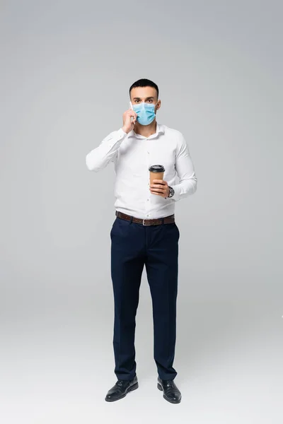 Ganzkörperansicht des hispanischen Geschäftsmannes mit Kaffee zum Reden auf dem Handy in grau — Stockfoto