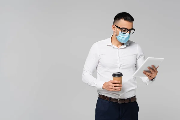 Jeune gestionnaire hispanique en masque médical tenant ordinateur portable et café pour aller isolé sur gris — Photo de stock