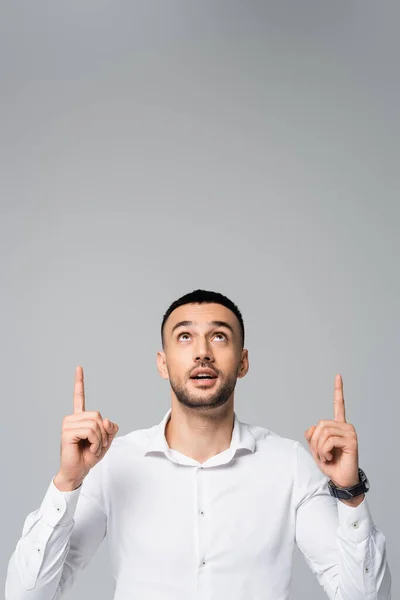 Young hispanic businessman looking up and pointing with fingers isolated on grey — Stock Photo