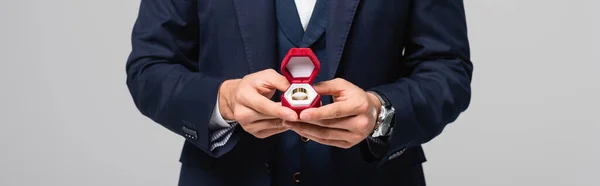 Partial view of man in suit holding jewelry box with wedding ring isolated on grey, banner — Stock Photo