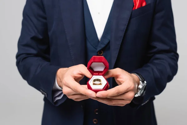 Cropped view of elegant man holding jewelry box with wedding ring isolated on grey — Stock Photo
