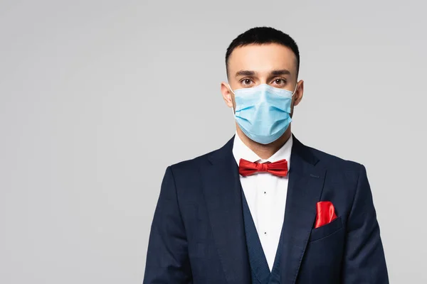 Jeune homme hispanique en costume bleu élégant et masque médical regardant la caméra isolée sur gris — Photo de stock