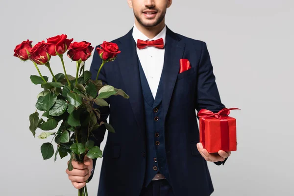 Vista parcial del hombre elegante con regalo de San Valentín y rosas rojas aisladas en gris — Stock Photo