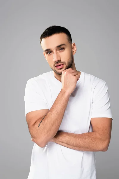 Nachdenklicher hispanischer Mann in weißem T-Shirt, der die Kamera isoliert auf grau schaut — Stockfoto