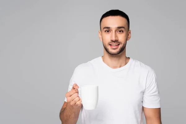 Smiling hispanic man in t-shirt holding white cup isolated on grey — Stock Photo