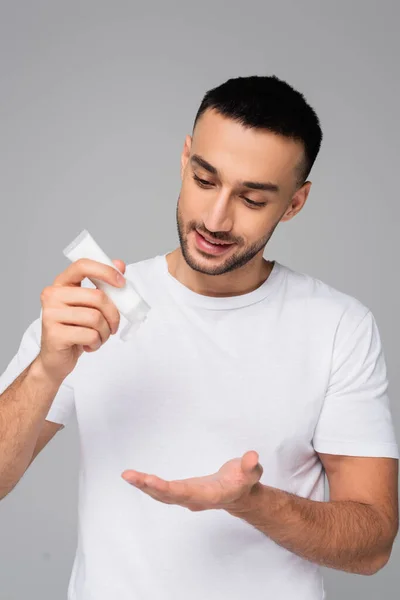 Morena hispano hombre celebración tubo de crema de manos aislado en gris - foto de stock