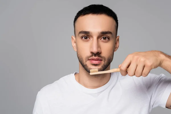 Junger hispanischer Mann blickt in die Kamera, während er die Zahnbürste isoliert auf grau hält — Stockfoto