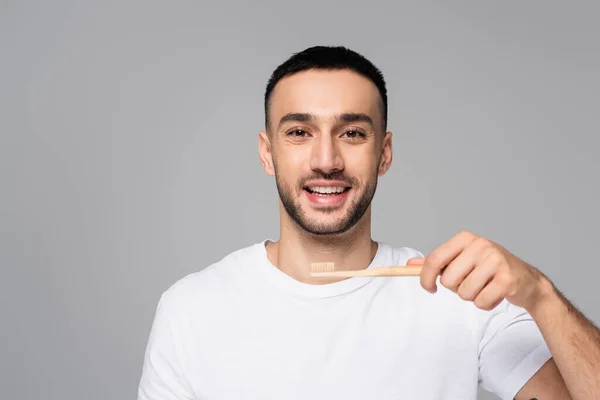 Glücklicher hispanischer Mann lächelt in die Kamera, während er die Zahnbürste isoliert auf grau hält — Stockfoto