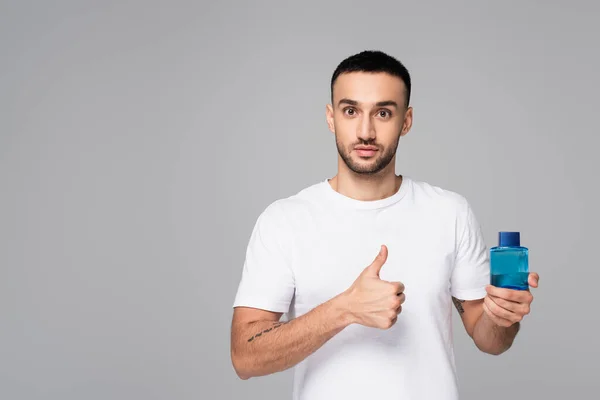 Morena hispano hombre mostrando el pulgar hacia arriba mientras celebración toilette agua aislado en gris - foto de stock