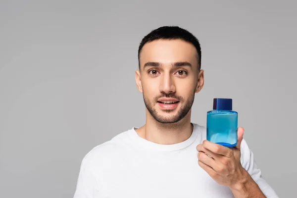 Brunette hispanic man holding vial of eau de cologne and looking at camera isolated on grey — Stock Photo