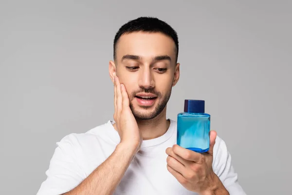 Brunette hispanic man applying aftershave lotion on face isolated on grey — Stock Photo