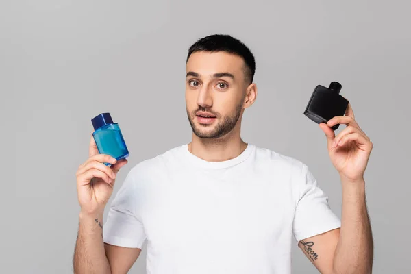 Young hispanic man in white t-shirt holding bottles of cologne water isolated on grey — Stock Photo