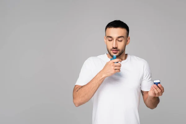 Hispanique homme sentant l'eau de Cologne avec les yeux fermés isolé sur gris — Photo de stock