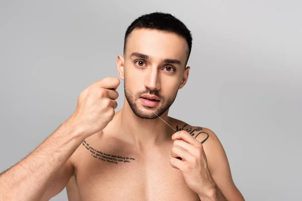 Hispanic shirtless tattooed man holding dental floss isolated on grey — Stock Photo