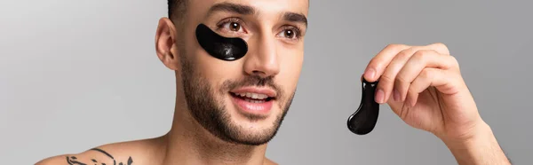 Giovane uomo ispanico sorridente che tiene la benda dell'occhio isolata sul grigio, striscione — Foto stock