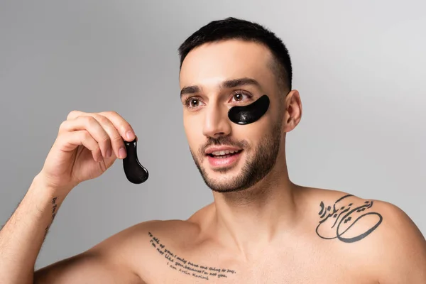 Hombre hispano barbudo tatuado sosteniendo parche ocular aislado en gris - foto de stock