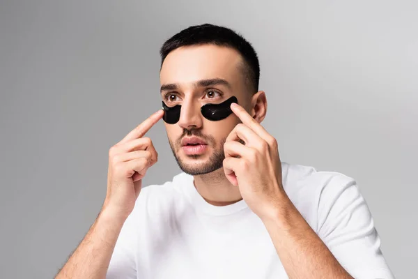 Jovem hispânico aplicando manchas oculares isoladas em cinza — Fotografia de Stock