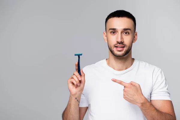 Brunette hispanic man in white t-shirt pointing at safety razor isolated on grey — Stock Photo