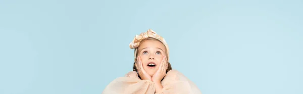 Amazed girl with hands near cheeks looking up isolated on blue, banner — Stock Photo